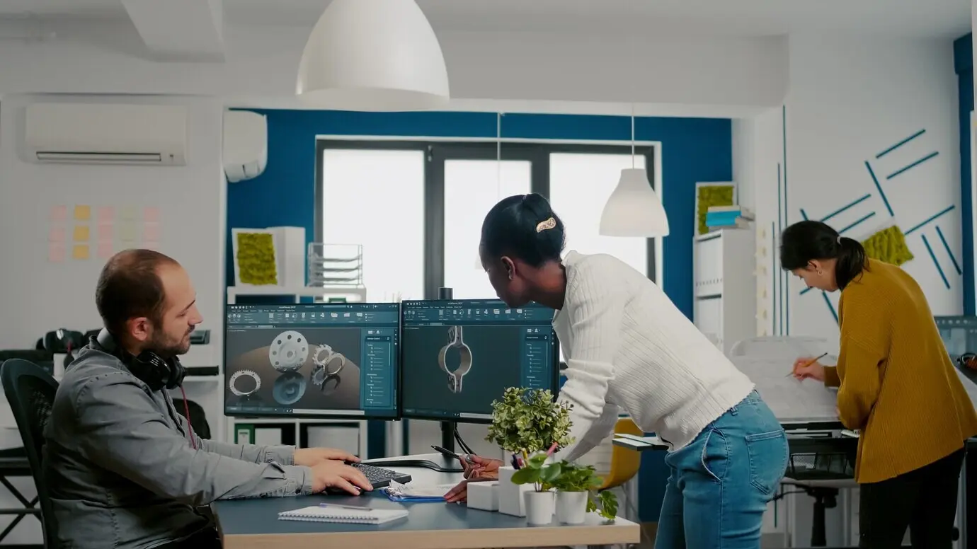 Многонациональная команда обменивается идеями о промышленном проекте, используя два монитора с d шестернями и металлическими ...